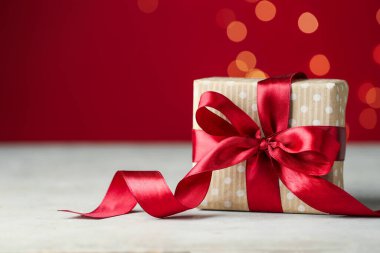 Sevgililer Günün kutlu olsun. Kırmızı arkaplan karşısında beyaz masadaki hediye kutusu bulanık ışıklarla, yakın plan