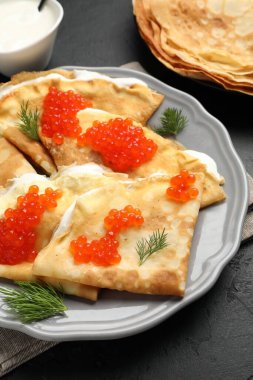 Kırmızı havyarlı leziz krepler ve siyah desenli masaya ekşi krema, yakın plan.