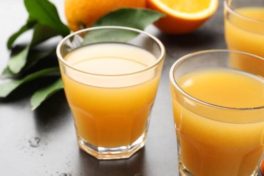 Taze portakal suyu, meyveler ve yapraklar gri masada, yakın plan.