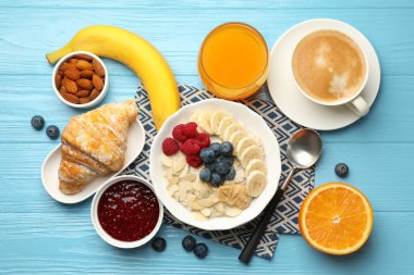 Sağlıklı kahvaltı. Fındıklı yulaf ezmesi, muz, böğürtlen, reçel, kahve ve meyve suyu açık mavi ahşap masada servis edilir.
