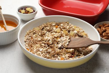 Tahıl yapıyorum. Bir kase yulaf ezmesi, bal ve kuru meyveler açık gri masada, yakın plan.