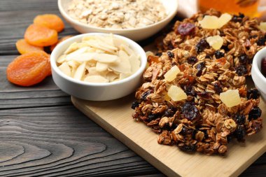 Kurumuş meyveli lezzetli granola barlar ve siyah ahşap masada fındıklar, yakın plan.