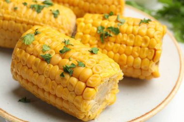 Beyaz masada maydanozlu haşlanmış mısır koçanı parçaları, yakın plan.