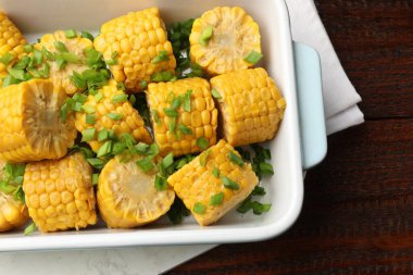 Ahşap masada, yeşil soğanlı haşlanmış mısır koçanı parçaları.