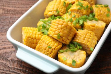 Haşlanmış mısır koçanı parçaları ve ahşap masada yeşil soğan, yakın plan.