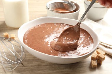 Ahşap masada kaşıkla çikolata hamuru alan kadın, yakın plan.