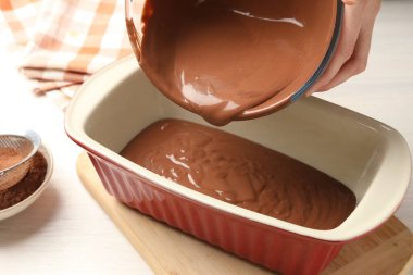 Kadın hafif ahşap masadaki yemek kabına çikolata hamuru döküyor, yakın plan.