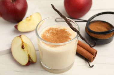 Bardakta lezzetli protein karışımı, tarçın, elma ve vanilya kapsülleri beyaz ahşap masada, yakın plan.