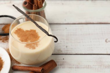 Bardakta lezzetli protein karışımı, beyaz ahşap masada tarçın ve vanilya kapsülü, yakın plan. Metin için boşluk