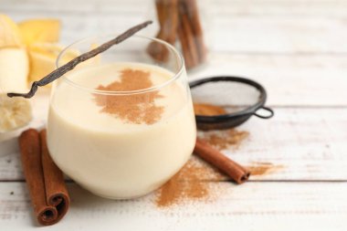 Bardakta lezzetli protein karışımı, tarçın, muz ve vanilya kapsülü beyaz ahşap masada, yakın plan. Metin için boşluk