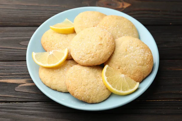Lezzetli limonlu kurabiyeler ve siyah ahşap masada meyve dilimleri, yakın plan.