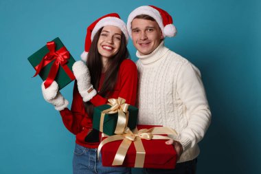 Noel Baba şapkalı mutlu çift açık mavi arka planda Noel hediyeleri ile