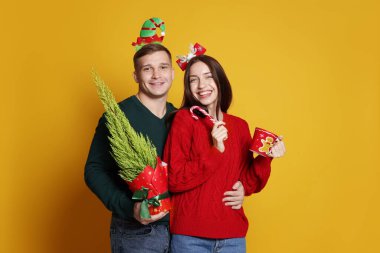 Yılbaşı bantlı mutlu çift sarı arka planda thuja ağacı, fincan ve şeker kamışı ile