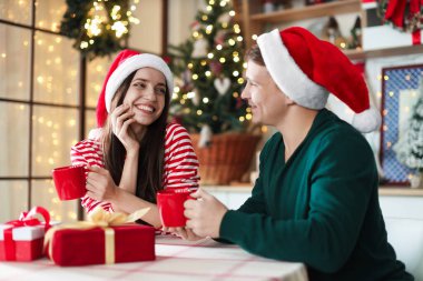 Noel Baba şapkalı mutlu çift evde bir bardak sıcak içecekle. Noel atmosferi