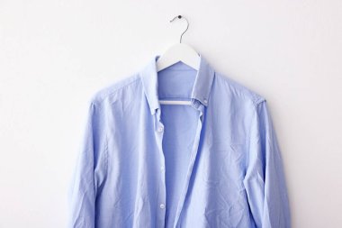 Beyaz duvarda asılı açık mavi buruşuk gömlek
