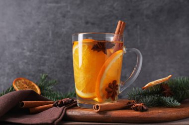 Cam bardaktaki lezzetli şarap, baharatlar, portakal dilimleri ve köknar dalları gri arka planda, yakın planda.