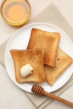 Tost ekmeği, tereyağı ve bal dilimleri bej masada, düz yerde.