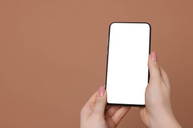 Kahverengi arka planda boş ekranlı akıllı telefonu olan bir kadın, yakın plan. Tasarım için model