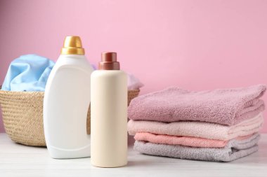 Çamaşır sepeti ve beyaz ahşap masada pembe arka planda duran deterjan şişeleri.