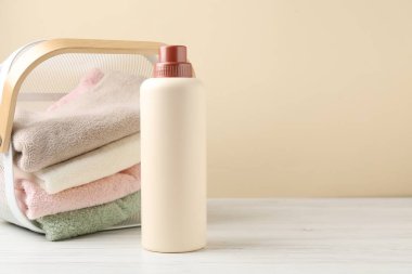 Çamaşır sepetinde havlular ve beyaz ahşap masa üzerinde bir şişe deterjan bej arka planda, mesaj için boşluk