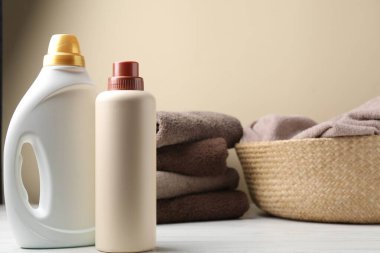 Çamaşır sepetinde havlular ve beyaz ahşap masadaki deterjan bej arka planda, yakın plan.