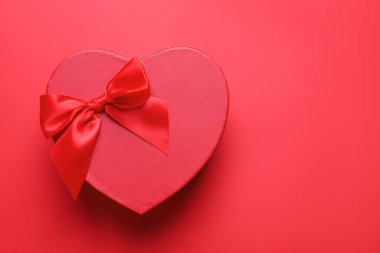 Sevgililer Günün kutlu olsun. Kırmızı arka planda kalp şeklinde hediye kutusu, üst manzara. Metin için boşluk