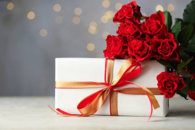 Sevgililer Günün kutlu olsun. Armağan kutusu ve kırmızı gül buketi beyaz masada gri arka planda bulanık ışıklarla, yakın plan. Metin için boşluk