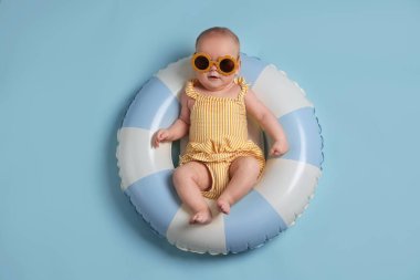 Şişirilebilir halkada güneş gözlüklü şirin bir bebek açık mavi arka planda, üst tarafta.