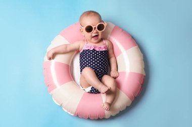 Şişirilebilir halkada güneş gözlüklü şirin bir bebek açık mavi arka planda, üst tarafta.