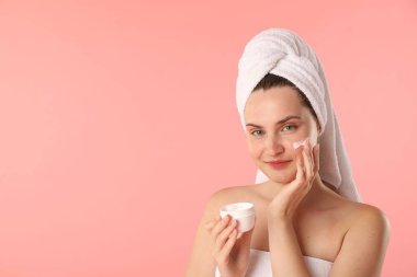Havluya sarılı güzel bir kadın pembe arka plana krem sürüyor. Metin için boşluk