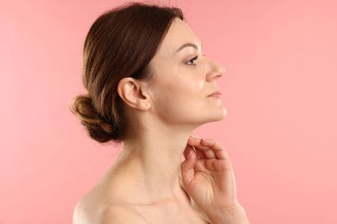 Kadın pembe arka planda boynuna dokunuyor.