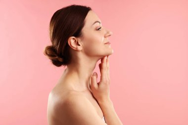 Kadın pembe arka planda boynuna dokunuyor.