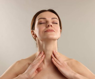 Açık gri arka planda boyun masajı yapan kadın.