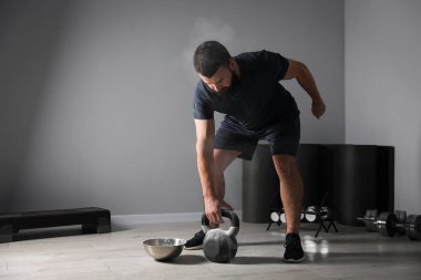 Güçlü adam spor salonunda kettlebell ile egzersiz yapıyor, mesaj için yer var.