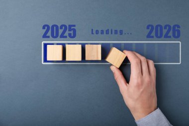 Yeni yıl 2026. Gri arka planda, yükleme çubuğuna tahtadan küpü diğerlerinin yanına koyan adam, üst görünüm