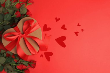 Kırmızı gül buketi, hediye kutusu ve kırmızı arka planda kalpler, üst manzara. Romantik tebrik kartı.