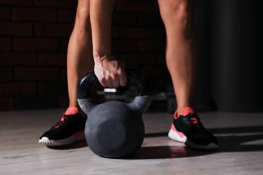 Woman exercising with kettlebell in dark gym, closeup