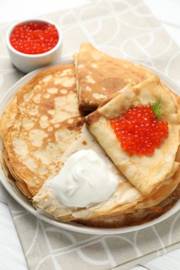 Kırmızı havyarlı leziz krepler ve beyaz ahşap masada ekşi krema, yakın plan.