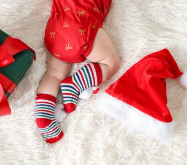 Noel çoraplı bebek, Noel Baba şapkası ve hediye kutusu yatakta, üst tarafta.