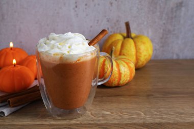 Cam bardakta kremalı balkabaklı latte, tarçın çubukları, taze sebzeler ve ahşap masada yanan mumlar, yakın plan. Metin için boşluk