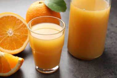 Taze portakal suyu ve meyveler gri masada, yakın plan.