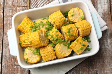 Ahşap masada, yeşil soğanlı haşlanmış mısır koçanı parçaları.