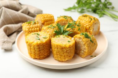 Beyaz mermer masada maydanozlu haşlanmış mısır koçanı parçaları, yakın plan.