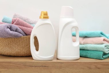 İçerideki beyaz duvarın yanındaki ahşap dolapta havlu ve şişe deterjan dolu çamaşır sepeti.