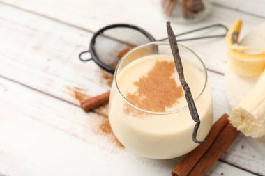 Bardakta lezzetli protein karışımı, tarçın, muz ve vanilya kapsülü beyaz ahşap masada, yakın plan. Metin için boşluk