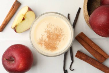 Bardakta lezzetli protein karışımı, tarçın, beyaz fayanslı masada elmalar ve vanilya kapsülleri.