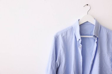 Beyaz duvarda asılı açık mavi buruşuk gömlek. Metin için boşluk