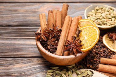 Ahşap masada sıcak şarap için farklı baharatlar ve portakal dilimleri, yakın plan. Metin için boşluk