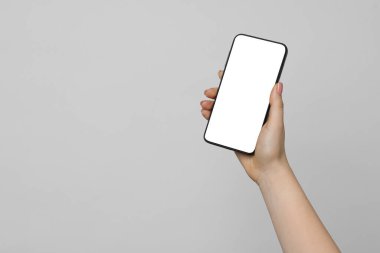 Açık gri arka planda boş ekranlı akıllı telefonu olan bir kadın, yakın plan. Tasarım için model
