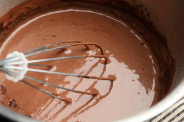 Liquid chocolate dough in bowl and whisk on table, closeup